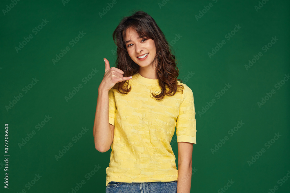 Call me gesture. Friendly modern smiling young girl offering contact communication by phone on green studio background Call me gesture. Friendly modern smiling young girl offering contact communication by phone on green studio background