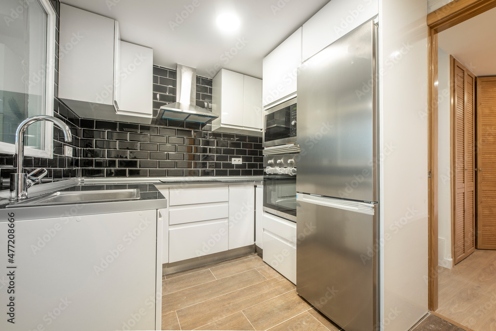 Fototapeta premium kitchen with white cabinets white brick wall black tiles and aluminum appliances leading to an office with venetian cabinets
