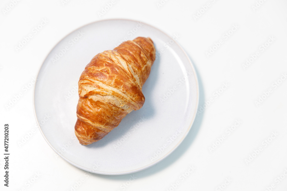 Freshly baked croissant on gray round plate on white background