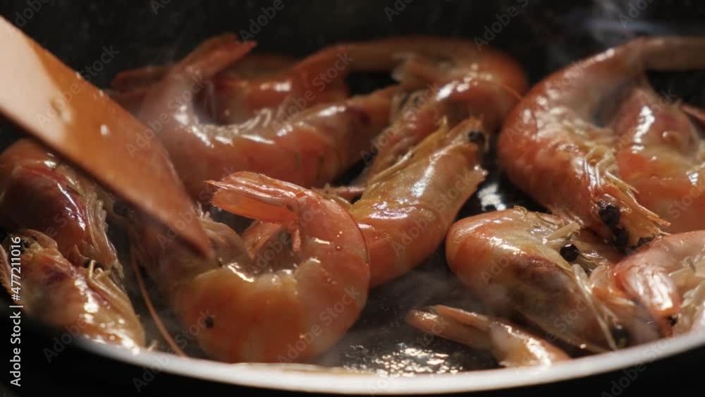 Shrimp in a shell in a pan close-up. The cook turns over with a wooden spatula Shrimp in a shell in a pan close-up. The cook turns over with a wooden spatula
