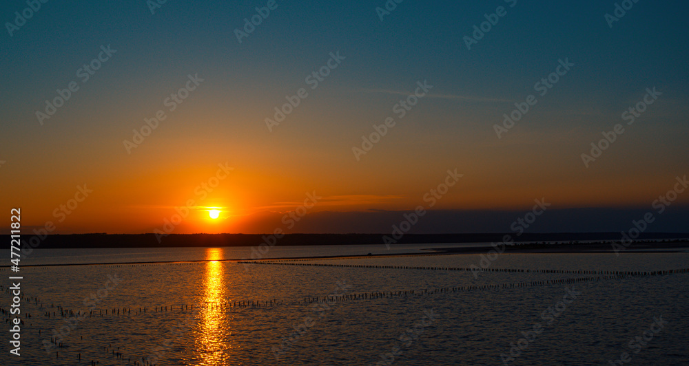 Panoramic seashore view with dramatic golden sunset. Calm beach in background.