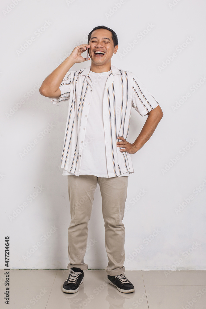 Full body portrait of cheerful asian man laughing while making a call isolated on white background Full body portrait of cheerful asian man laughing while making a call isolated on white background