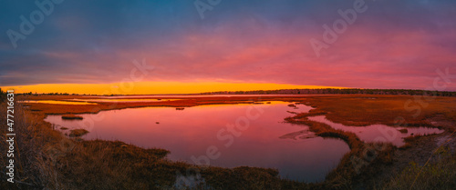 Sunrise panoramic seascape over the marsh pond in Mashpee on South Cape Beach, Massachusetts. Pink and blue western sky and water reflections at cloudy dawn.