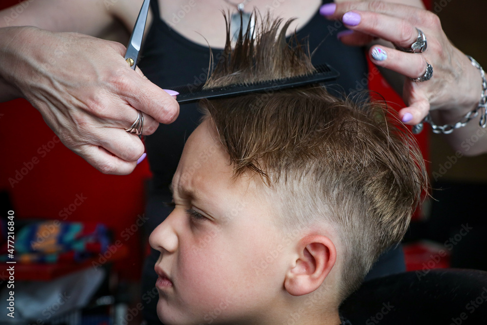 Fototapeta premium Funny Frowning Little Boy At The Hairdresser