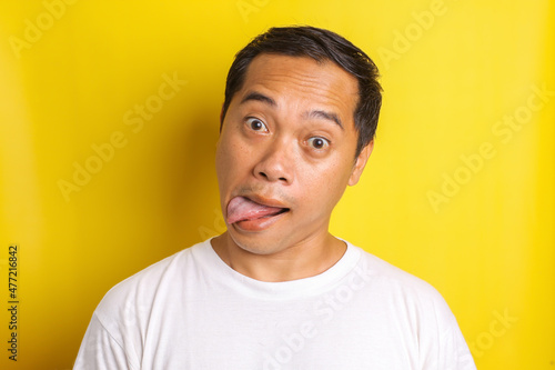 Close-up portrait of asian man with mocking expression, reproaching, and sticking out tongue isolated on yellow background © Gatot