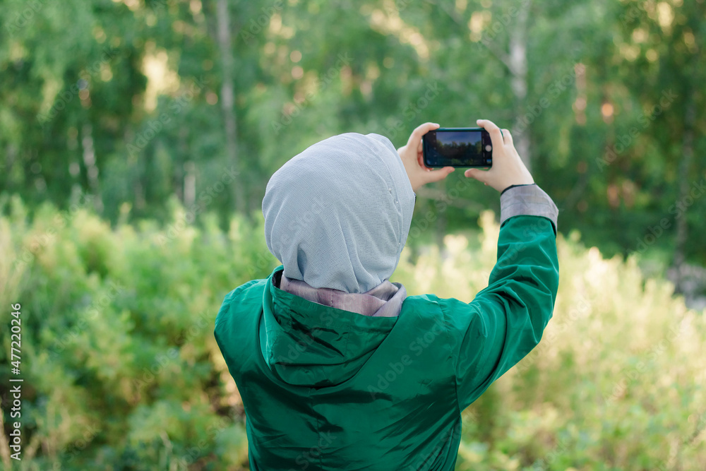 Fototapeta premium A Muslim woman in a blue hijab takes pictures of nature in the forest.