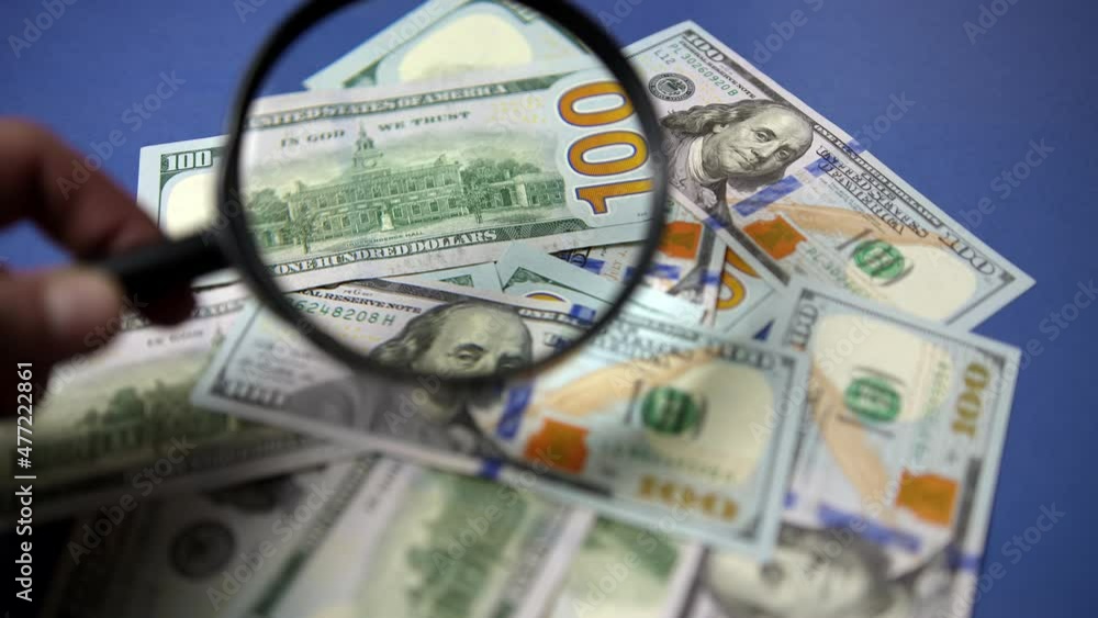 checking 100 banknotes for counterfeiting through a magnifying glass. Finance and Investment Concept. Money Cash.