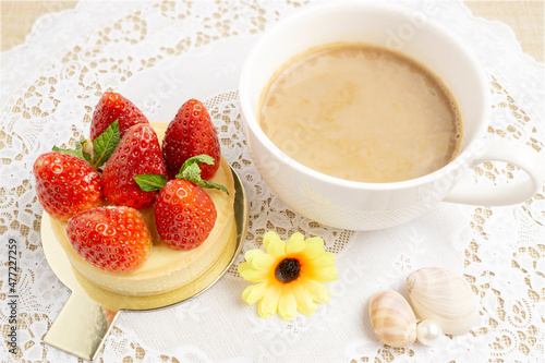 Tasty strawberry cheese tart topping with fresh strawberries and green leaves served with hot coffee on white lace placemat