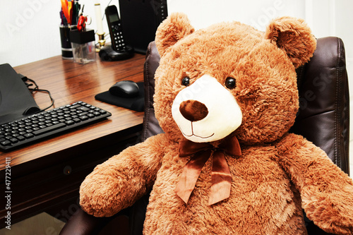 Oso de peluche café sentado en una silla de oficina. Trabajando en un escritorio de madera en casa. Concepto de trabajo en casa. photo