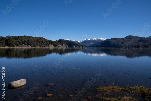 View of the lake in a sunny day. The forest, mountains and blue sky reflection in the water surface. 