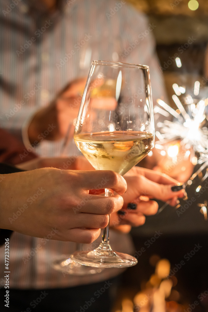 Close up on hands of group of people holding glasses of wine and sparkles while toasting and celebrating indoor focus on glass of wine birthday or new year celebration concept