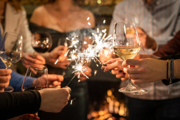 Close up on hands of group of people holding glasses of wine and sparkles while toasting and celebrating indoor focus on glass of wine birthday or new year celebration concept