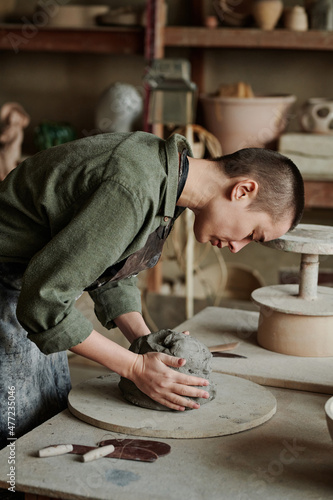 Young woman in apron concentrating on her work at the table, she making ceramic sculptures with clay
