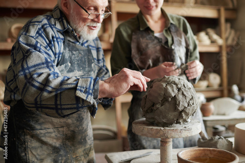 Canvas Print Senior potter in eyeglasses using stick to make form from piece of clay, he teac