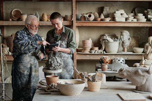 Canvas Print Senior sculptor pointing at tablet pc and showing his assistant the ceramic scul