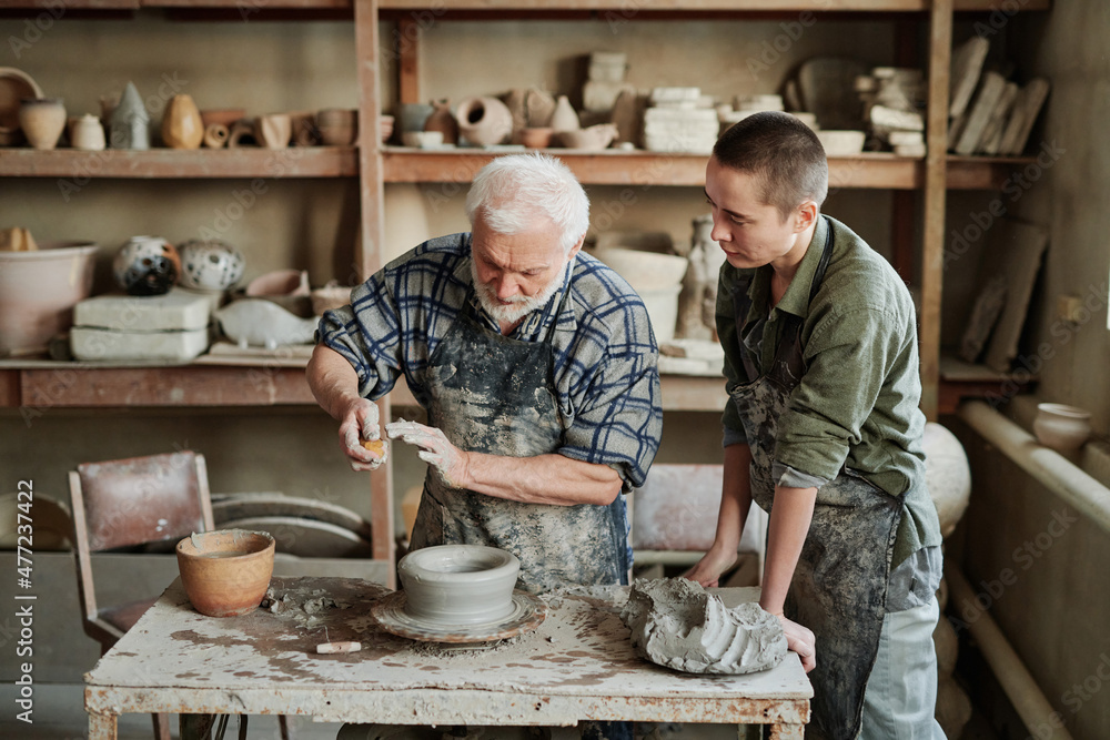 Senior man showing the process of making ceramic vases to his assistant in the pottery workshop Senior man showing the process of making ceramic vases to his assistant in the pottery workshop