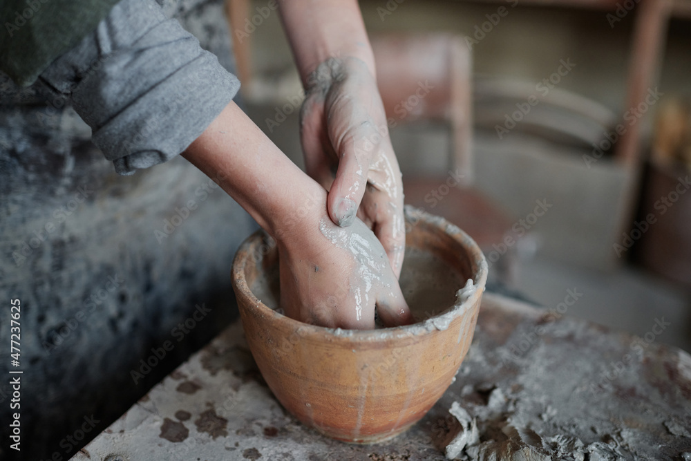 Fototapeta premium Close-up of pottery artist washing her hands of clay in bowl after work