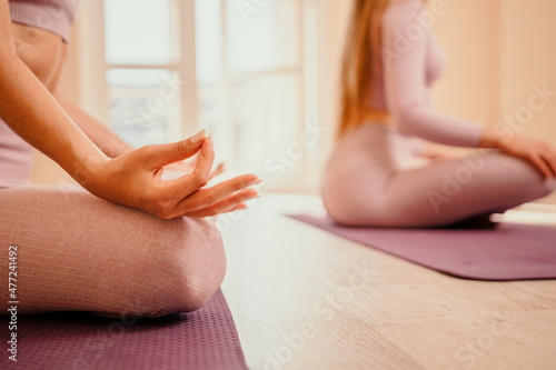 Two young sporty woman, fitness instructor in pink sportswear doing stretching and pilates on yoga mat in the studio with mirror. Female fitness yoga routine concept. Healthy lifestyle and harmony.