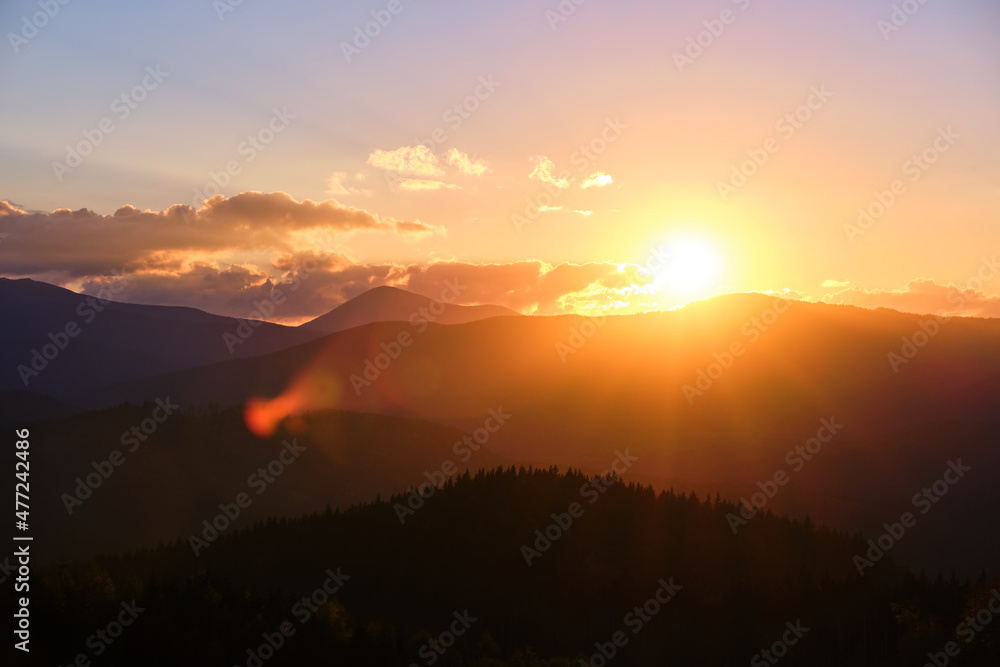 Beautiful evening panoramic landscape with bright setting sun over distant mountain peaks at sunset Beautiful evening panoramic landscape with bright setting sun over distant mountain peaks at sunset