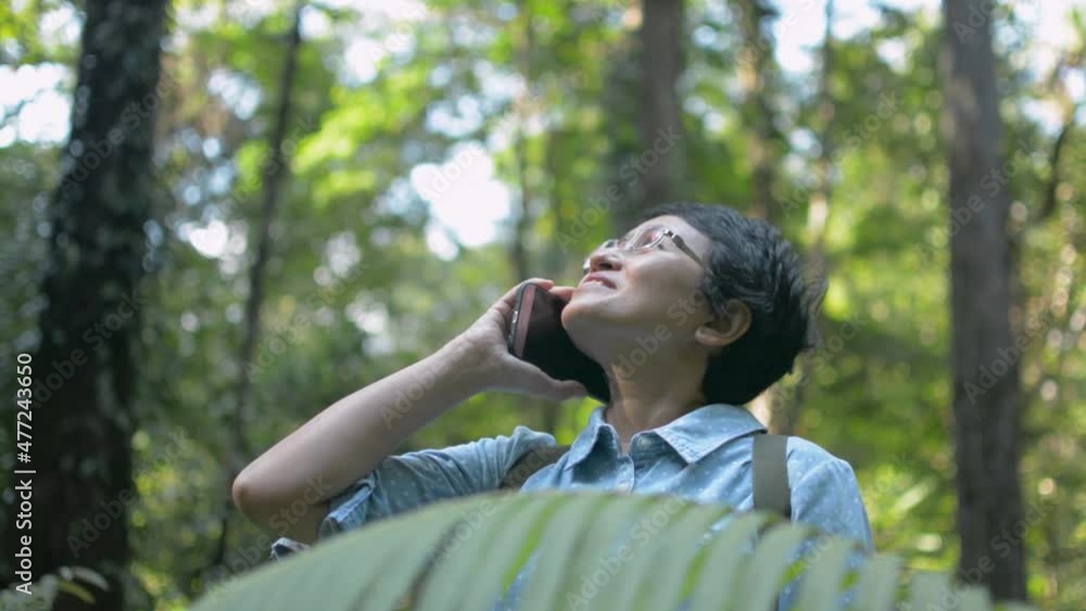 Asian woman nature explorer using mobile smartphone talking to her family while trekking in the forest. Signal network for comprehensive communication. Wireless connectivity technology. Asian woman nature explorer using mobile smartphone talking to her family while trekking in the forest. Signal network for comprehensive communication. Wireless connectivity technology.