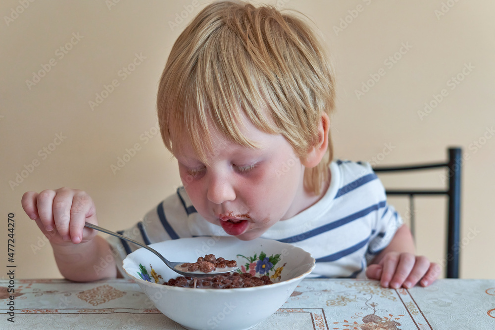 Little boy is having breakfast with chocolate balls with milk Little boy is having breakfast with chocolate balls with milk