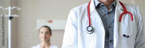 Doctor with stethoscope around neck holding clipboard with documents on background of patient