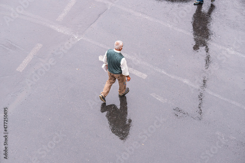 An elderly man walking on the street in the rain