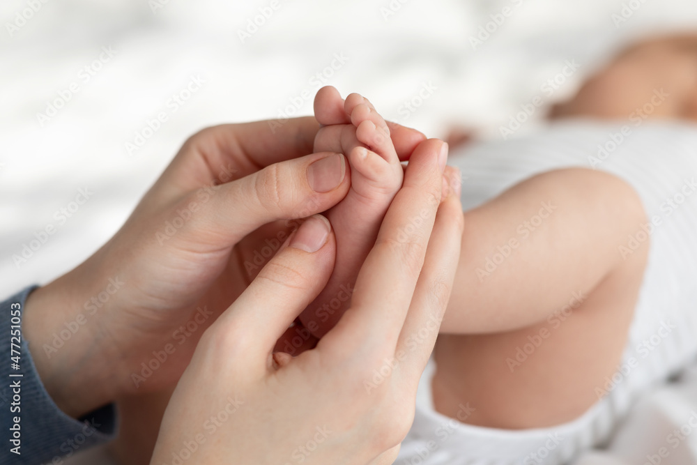 Child Care. Mother Massaging Tiny Feets Of Her Newborn Baby, Closeup Shot