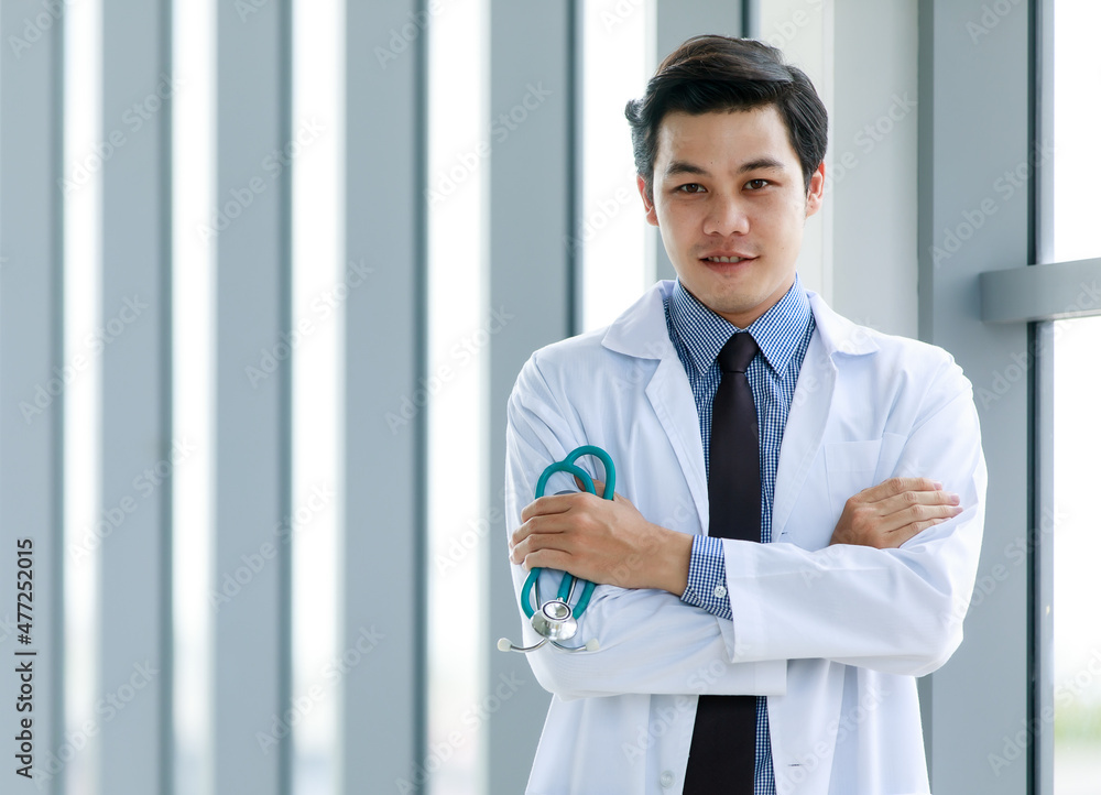 Professional Asian physician man in formal business uniform of clinical hygiene gown smiling and standing with arm crossed and medical stethoscope in hand as confident on career expertise Professional Asian physician man in formal business uniform of clinical hygiene gown smiling and standing with arm crossed and medical stethoscope in hand as confident on career expertise