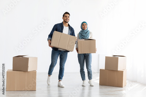 Young muslim couple moving to new apartment, holding paper boxes