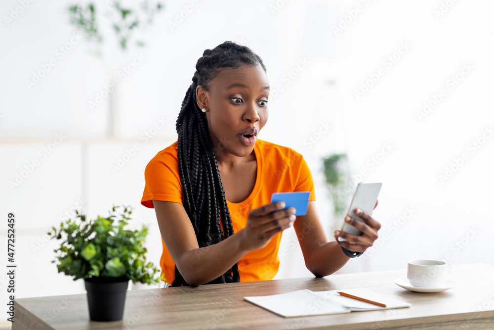 Black lady with credit card looking at smartphone in shock, finding huge online sale, shopping remotely from home Black lady with credit card looking at smartphone in shock, finding huge online sale, shopping remotely from home
