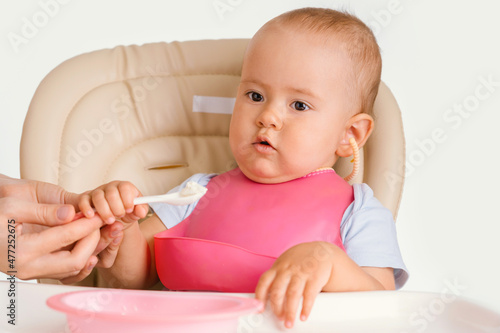 Feeding the baby with a spoon. Toddler sits on a chair while feeding
