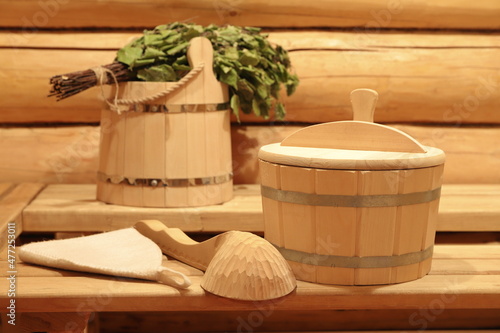 Traditional sauna accessories and birch broom are on a wooden benches in the interior of the bath. 