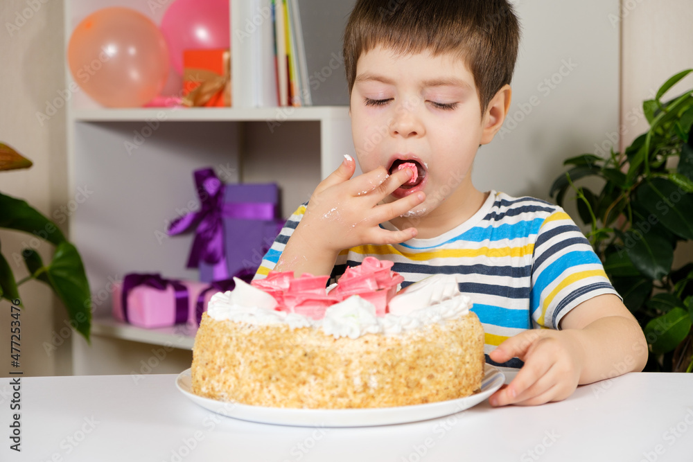 A happy boy eats a birthday cake, eats with his hands and licks his fingers. A happy boy eats a birthday cake, eats with his hands and licks his fingers.