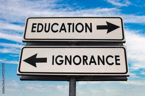 Education versus ignorance road sign with two arrows on blue and grey sky background. White two street sign with arrows on metal pole. Two way road sign with text.