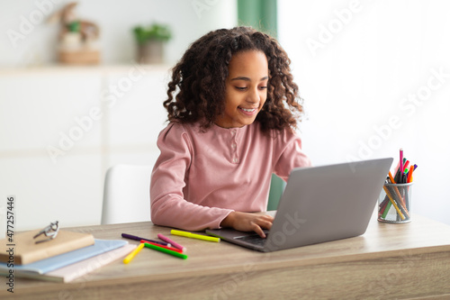Homeschooling concept. Happy black girl studying at home with laptop  typing on keyboard  sitting in living room