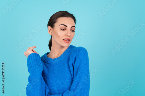 Young woman in a blue knitted sweater and natural daytime makeup on a turquoise background, plump lips with nude matte lipstick, looks down to the side