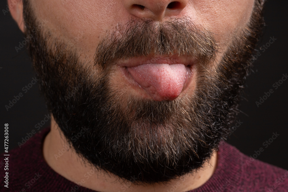 Obraz premium Cropped photo closeup of funny man grimacing at camera with sticking out his tongue isolated over black background.