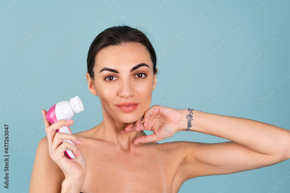 Close-up beauty portrait of topless woman with perfect skin and natural makeup, full nude lips, holding an electric facial brush. Facial cleansing with microvibrations Close-up beauty portrait of topless woman with perfect skin and natural makeup, full nude lips, holding an electric facial brush. Facial cleansing with microvibrations