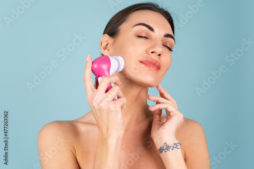 Close-up beauty portrait of topless woman with perfect skin and natural makeup, full nude lips, holding an electric facial brush. Facial cleansing with microvibrations