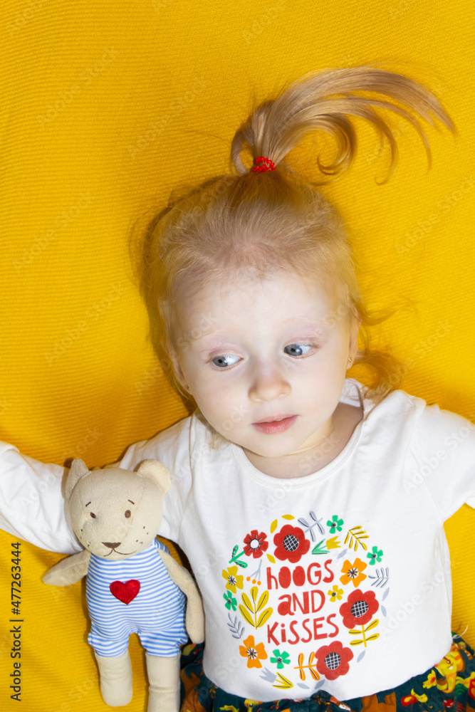 A small, red-haired girl is laughing at home on a gray sofa with purple pillows and a yellow background. A small, red-haired girl is laughing at home on a gray sofa with purple pillows and a yellow background.