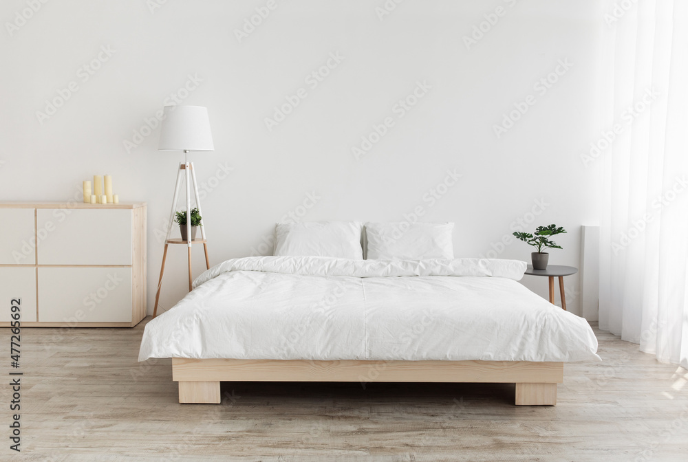 Real photo of bedroom interior in simple style. Big bed with pillows, lamp and furniture, white wall, empty space