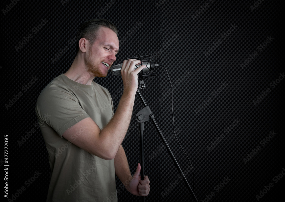 Young caucasian man singing in front of black soundproofing walls. Musicians producing music in professional recording studio. Young caucasian man singing in front of black soundproofing walls. Musicians producing music in professional recording studio.