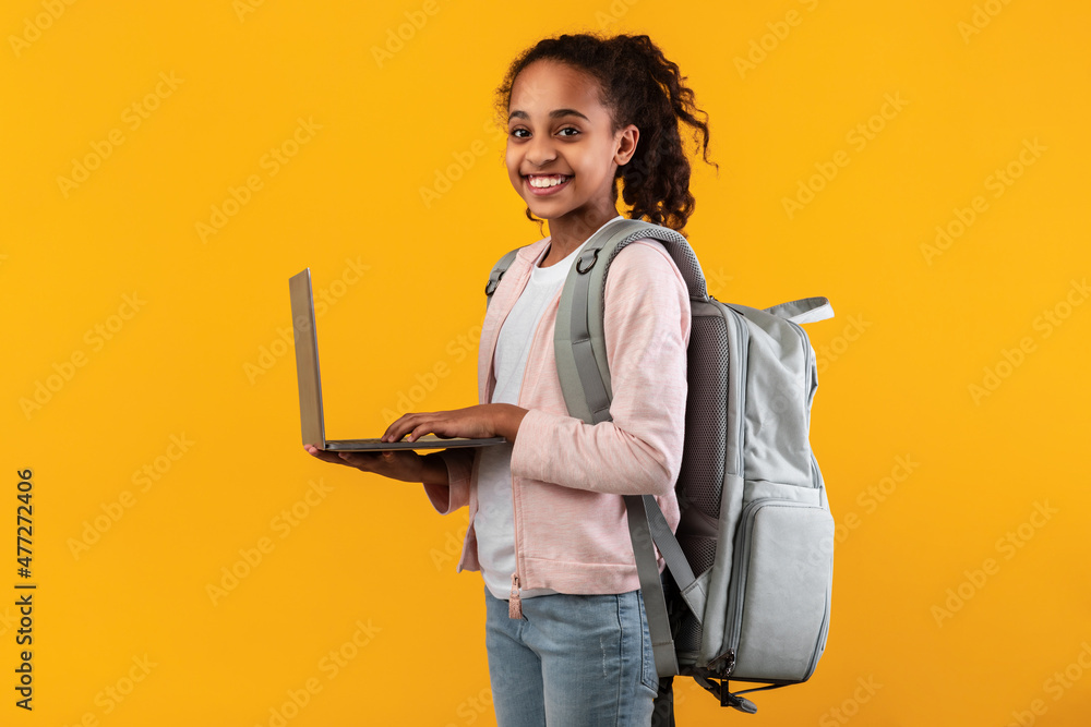 Black girl standing with personal computer at yellow studio