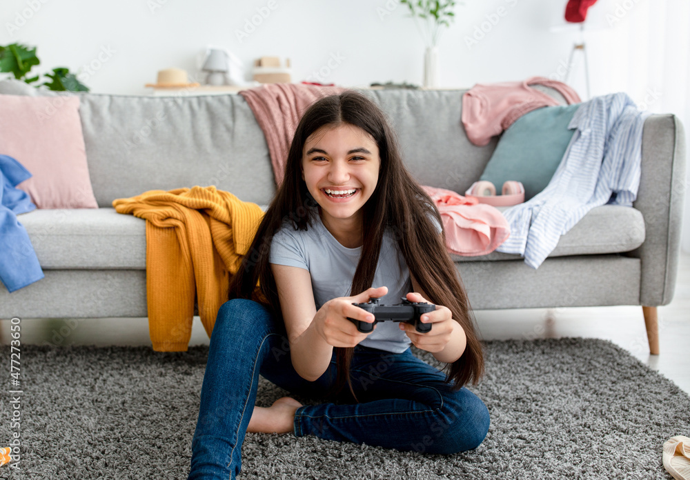 Having fun at home. Happy Indian teenage girl playing online video games, sitting on floor with controller, indoors Having fun at home. Happy Indian teenage girl playing online video games, sitting on floor with controller, indoors