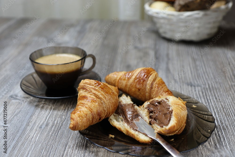 Croissants with chocolate cream and coffee on the rustic wooden background. Closeup