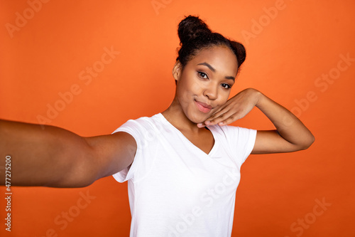 Photo of young pretty african woman arm touch chin make selfie recor video isolated over orange color background photo