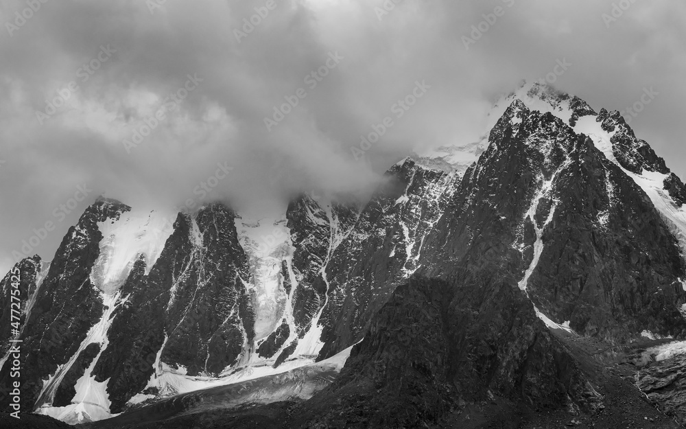 Monochrome dramatic landscape with big snowy mountain peaks above low clouds. Atmospheric large snow mountain tops in cloudy sky.