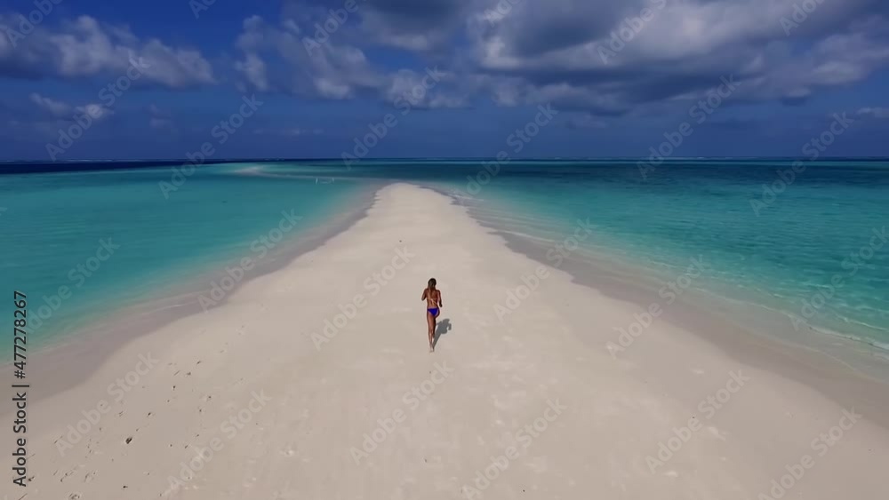 Beautiful tanned girl dressed in a blue bikini runs along the shore Maldives island. Flight with drone Beautiful tanned girl dressed in a blue bikini runs along the shore Maldives island. Flight with drone