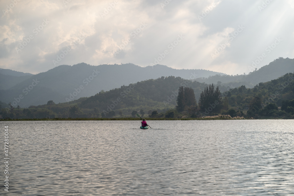 Fototapeta premium Kayaks in the lake. Tourists kayaking on mirror lake. taking photo when travel activity. woman playing in water in sunset. active woman rowing boat in lake with mountain view in evening.